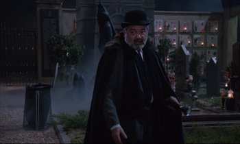 Movie still from “Voice of the Moon” (1990), directed by Richard Stanley – A man with a beard wearing a black hat and a cape; Medium shot, Over the shoulder angle