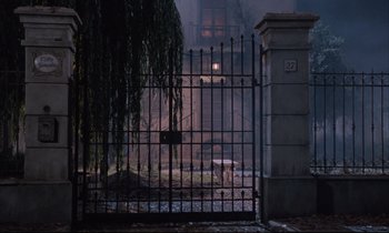 Movie still from “Voice of the Moon” (1990), directed by Richard Stanley – A view of a building through an iron gate; Wide shot, Low angle