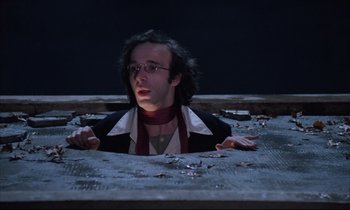 Movie still from “Voice of the Moon” (1990), directed by Richard Stanley – A man in a black jacket and a red tie; Medium shot, Overhead angle
