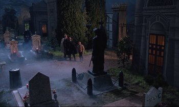 Movie still from “Voice of the Moon” (1990), directed by Richard Stanley – A group of people standing around a statue in a graveyard; Wide shot, High angle