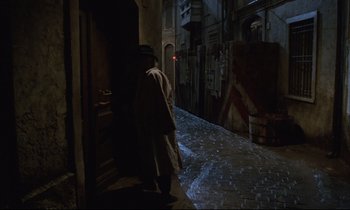 Movie still from “Voice of the Moon” (1990), directed by Richard Stanley – A man walking down a street at night; Wide shot, High angle