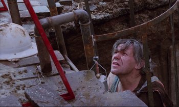 Movie still from “Voice of the Moon” (1990), directed by Richard Stanley – An old man is looking down at a pipe; Medium shot, Low angle
