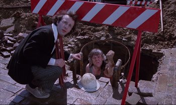 Movie still from “Voice of the Moon” (1990), directed by Richard Stanley – A man kneeling down next to a woman in a chair; Medium shot, High angle