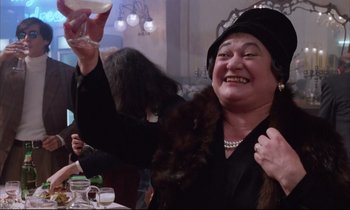 Movie still from “Voice of the Moon” (1990), directed by Richard Stanley – An older woman wearing a hat and holding a wine glass; Close Up shot, Low angle