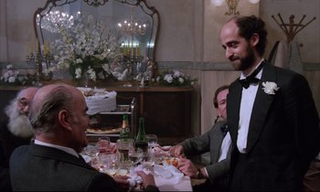 Movie still from “Voice of the Moon” (1990), directed by Richard Stanley – A group of people sitting at a table with wine glasses; Medium shot, Over the shoulder angle