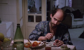 Movie still from “Voice of the Moon” (1990), directed by Richard Stanley – A man sitting at a dinner table eating food; Medium shot, High angle