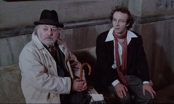 Movie still from “Voice of the Moon” (1990), directed by Richard Stanley – Two men sitting next to each other on a bench; Medium shot, High angle