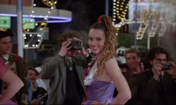 Movie still from “Voice of the Moon” (1990), directed by Richard Stanley – A woman in a purple dress is taking a picture; Medium shot, Over the shoulder angle