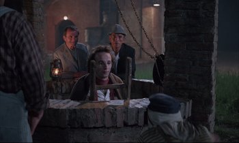 Movie still from “Voice of the Moon” (1990), directed by Richard Stanley – A group of people standing around a brick wall; Medium shot, Over the shoulder angle