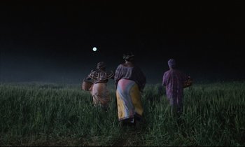 Movie still from “Voice of the Moon” (1990), directed by Richard Stanley – A group of people standing in a field at night; Extreme Wide shot, Low angle