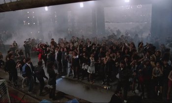 Movie still from “Voice of the Moon” (1990), directed by Richard Stanley – A large group of people standing in a room; Wide shot, High angle