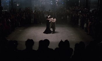 Movie still from “Voice of the Moon” (1990), directed by Richard Stanley – A couple of people that are dancing in front of a crowd; Wide shot, Overhead angle