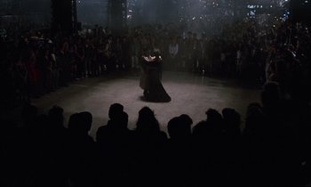 Movie still from “Voice of the Moon” (1990), directed by Richard Stanley – A couple of people that are dancing in front of a crowd; Extreme Wide shot, Overhead angle