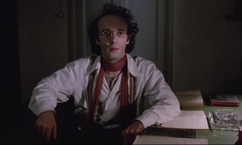 Movie still from “Voice of the Moon” (1990), directed by Richard Stanley – A man sitting in front of a table with papers on top of it; Close Up shot, Low angle