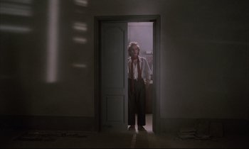 Movie still from “Voice of the Moon” (1990), directed by Richard Stanley – A man standing in a doorway in the dark; Wide shot, Low angle