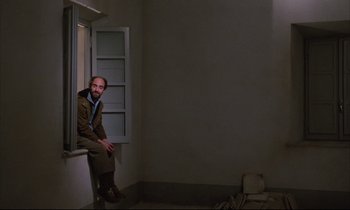 Movie still from “Voice of the Moon” (1990), directed by Richard Stanley – A man sitting on a windowsill in a dark room; Wide shot, Low angle