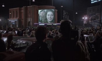 Movie still from “Voice of the Moon” (1990), directed by Richard Stanley – People are watching a movie on a big screen; Wide shot, Over the shoulder angle
