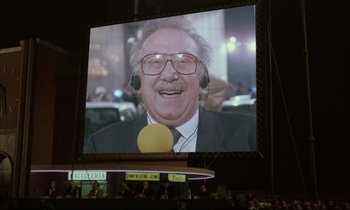 Movie still from “Voice of the Moon” (1990), directed by Richard Stanley – An old man with glasses and a mustache is on a big screen; Close Up shot, Low angle