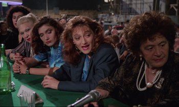 Movie still from “Voice of the Moon” (1990), directed by Richard Stanley – A group of women sitting at a table with microphones; Medium shot, High angle