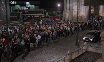 Movie still from “Voice of the Moon” (1990), directed by Richard Stanley – A crowd of people standing on the side of the street; Extreme Wide shot, High angle