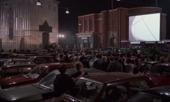 Movie still from “Voice of the Moon” (1990), directed by Richard Stanley – A group of people sitting in a parking lot watching a movie; Extreme Wide shot, High angle