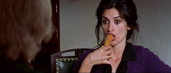 Movie still from “Volver” (2006), directed by Pedro Almodóvar – A beautiful woman eating a piece of food while sitting in a chair; Close Up shot, Over the shoulder angle
