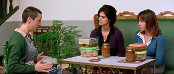 Movie still from “Volver” (2006), directed by Pedro Almodóvar – A woman sitting at a table in front of a stack of jars; Medium shot, Over the shoulder angle
