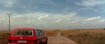 Movie still from “Volver” (2006), directed by Pedro Almodóvar – A red van driving down a dirt road near a wind farm; Extreme Wide shot, Low angle