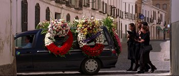 Movie still from “Volver” (2006), directed by Pedro Almodóvar – A black car with a bunch of wreaths on the back of it; Wide shot, Low angle