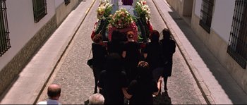 Movie still from “Volver” (2006), directed by Pedro Almodóvar – A group of people kneeling down next to a casket; Wide shot, High angle