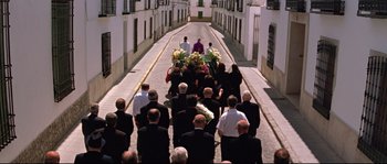 Movie still from “Volver” (2006), directed by Pedro Almodóvar – A group of people walking down a street with flowers; Extreme Wide shot, High angle