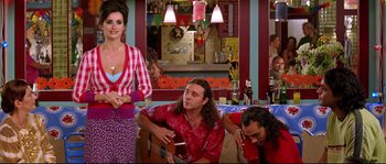 Movie still from “Volver” (2006), directed by Pedro Almodóvar – A group of people sitting in a room with a guitar; Medium shot, Over the shoulder angle