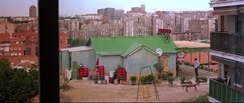 Movie still from “Volver” (2006), directed by Pedro Almodóvar – A building with a green roof in the middle of a city; Extreme Wide shot, High angle