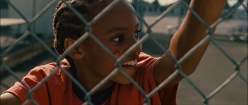 A young girl is looking through a fence