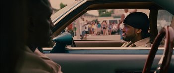 Movie still from “Waist Deep” (2006), directed by Vondie Curtis-Hall – A man driving a car in front of a group of onlookers; Close Up shot, Over the shoulder angle