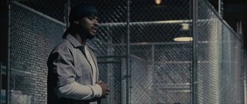 Movie still from “Waist Deep” (2006), directed by Vondie Curtis-Hall – A man standing in front of a chain link fence; Medium shot, Over the shoulder angle