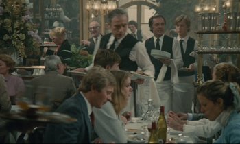 Movie still from “Waiter!” (1983), directed by Claude Sautet – A group of people standing around a table with plates; Medium shot, Over the shoulder angle