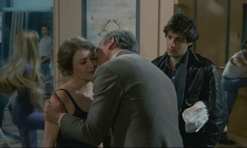 Movie still from “Waiter!” (1983), directed by Claude Sautet – A man and a woman kissing in front of another man; Medium shot, Over the shoulder angle