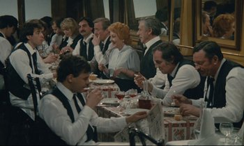 Movie still from “Waiter!” (1983), directed by Claude Sautet – A group of people sitting at a dinner table; Wide shot, High angle