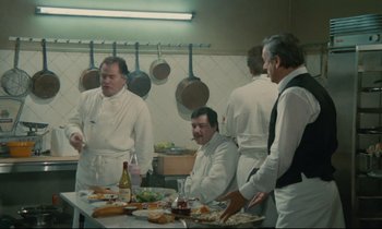 Movie still from “Waiter!” (1983), directed by Claude Sautet – A group of men standing around a table in a kitchen; Medium shot, High angle