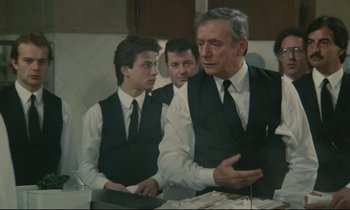 Movie still from “Waiter!” (1983), directed by Claude Sautet – A group of men in black vests and ties; Medium shot, Over the shoulder angle