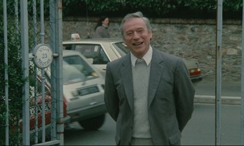 Movie still from “Waiter!” (1983), directed by Claude Sautet – An older man standing in front of a car; Medium shot, Over the shoulder angle