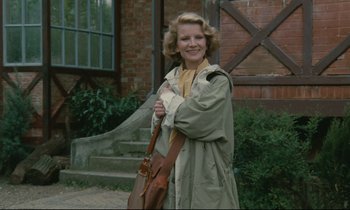 Movie still from “Waiter!” (1983), directed by Claude Sautet – A woman in a trench coat holding onto a purse; Medium shot, Low angle