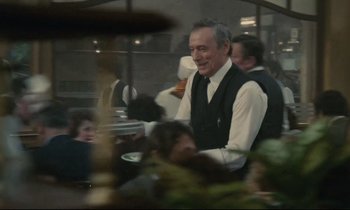 Movie still from “Waiter!” (1983), directed by Claude Sautet – A man wearing a black vest and a white tie; Medium shot, Over the shoulder angle