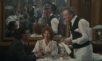 Movie still from “Waiter!” (1983), directed by Claude Sautet – A group of people sitting at a table in a restaurant; Wide shot, Over the shoulder angle
