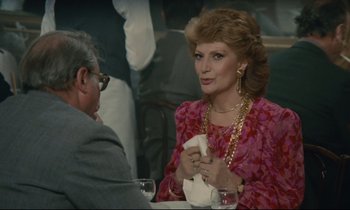 Movie still from “Waiter!” (1983), directed by Claude Sautet – An older woman sitting at a table with a man; Medium shot, Over the shoulder angle
