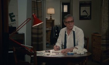 Movie still from “Waiter!” (1983), directed by Claude Sautet – A man sitting at a table writing on a piece of paper; Medium shot, Over the shoulder angle