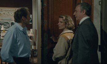 Movie still from “Waiter!” (1983), directed by Claude Sautet – A man and a woman standing next to each other in a room; Medium shot, Over the shoulder angle