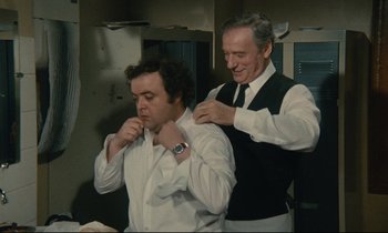 Movie still from “Waiter!” (1983), directed by Claude Sautet – A man helping another man put on a tie; Medium shot, Over the shoulder angle