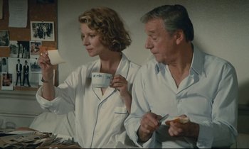 Movie still from “Waiter!” (1983), directed by Claude Sautet – A man and a woman sitting next to each other holding a cup; Medium shot, Low angle